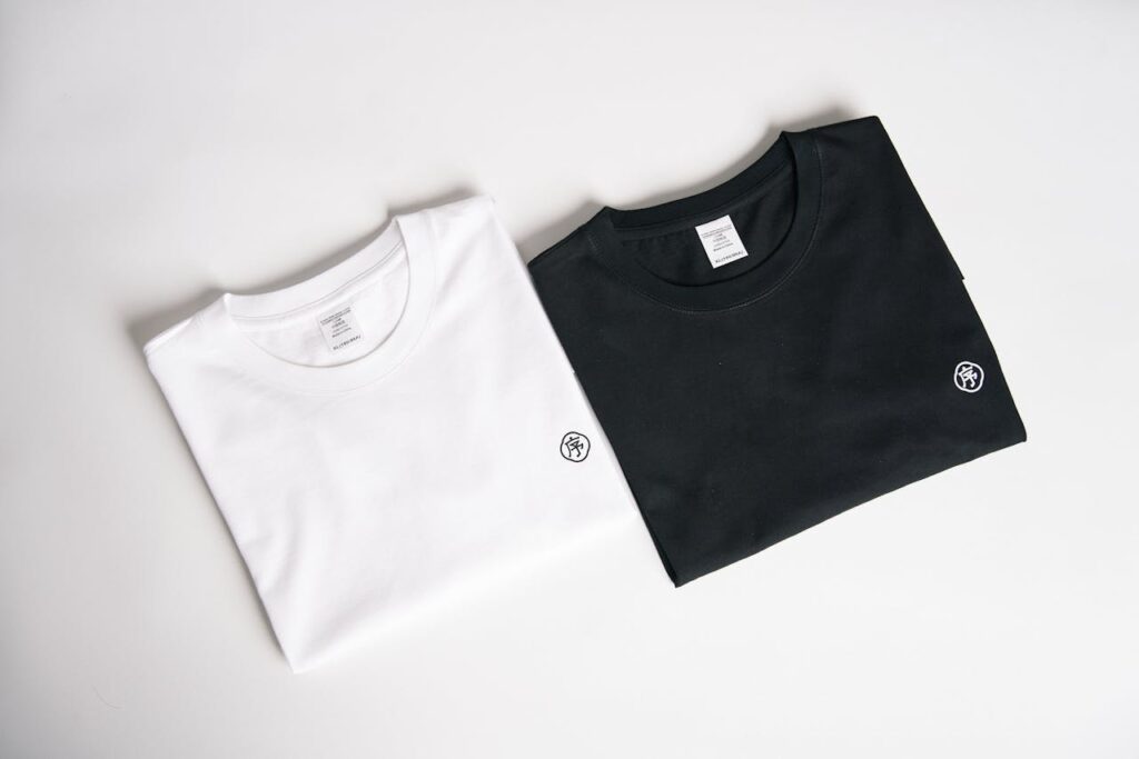 Two folded t-shirts, one black and one white, on a plain background in a minimalist style.