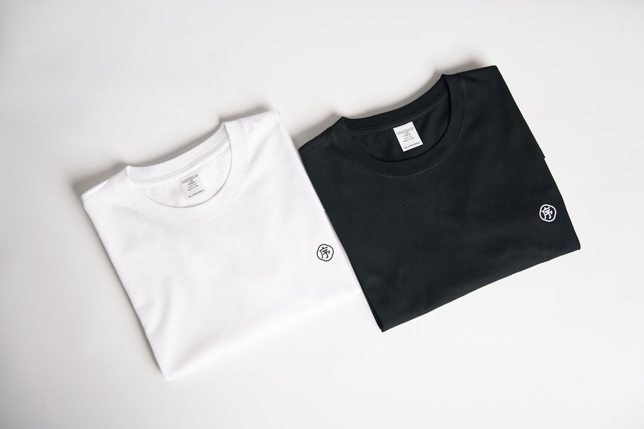 Two folded t-shirts, one black and one white, on a plain background in a minimalist style.